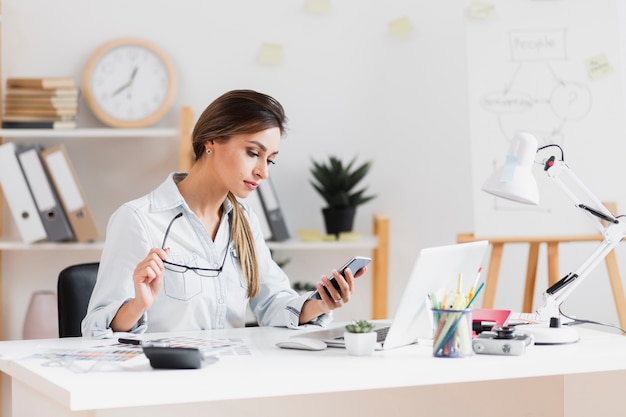 Mulher de negócios, segurando os óculos e olhando no telefone