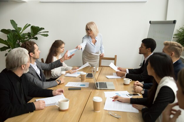 Mulher de negócios sênior, entregando o relatório financeiro ao gerente na reunião de equipe