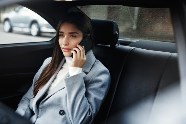 Mulher de negócios sentada no carro e falando ao telefone