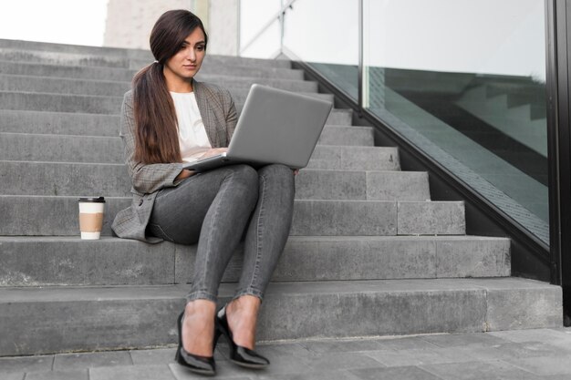Mulher de negócios trabalhando no laptop enquanto toma café nos degraus