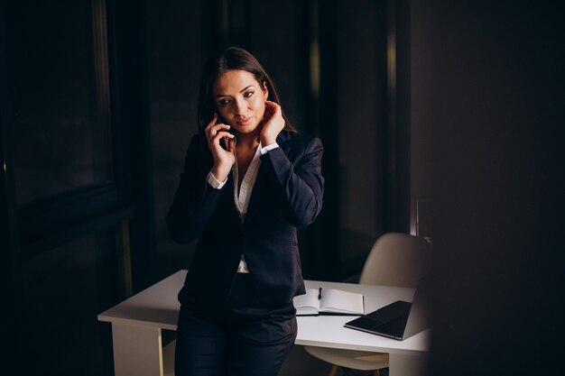 Mulher de negócios usando o telefone no escritório e ficando até tarde da noite