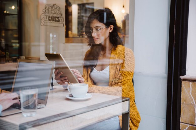Mulher de óculos usando tablet no café