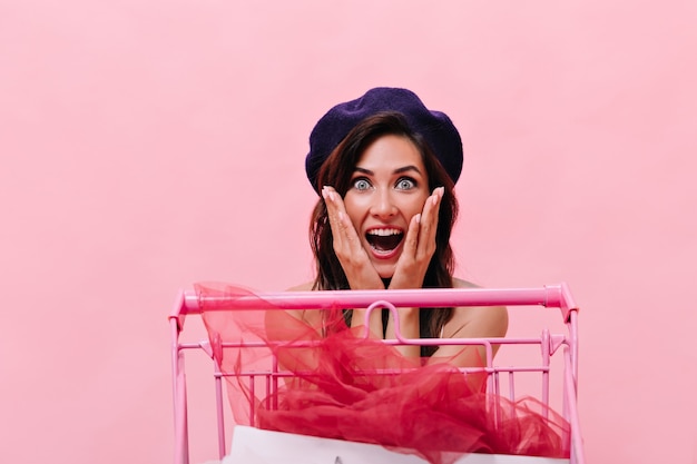 Foto grátis mulher de olhos azuis na boina preta olha para a câmera surpresa no fundo rosa. feliz linda garota com cabelo escuro, posando no isolado.