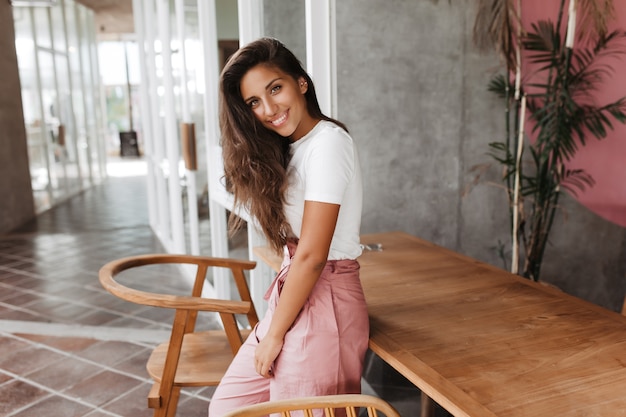 Mulher de olhos verdes, cabelos escuros e roupa elegante e clara sorrindo