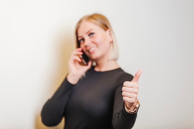 Mulher de pé segurando o telefone dando o polegar para cima