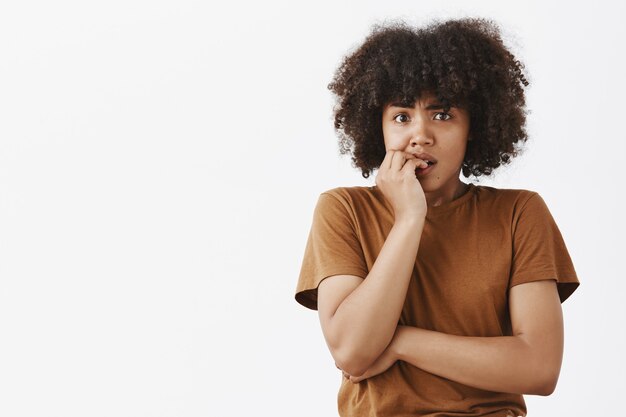 Mulher de pele escura, nervosa e em pânico, com penteado afro, roendo as unhas e olhando preocupada como se esperasse que coisas ruins acontecessem