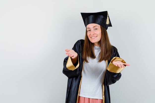 Mulher de pós-graduação em roupas casuais, uniforme, espalhando as palmas das mãos para a câmera e olhando alegre, vista frontal.