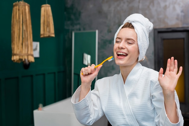 Mulher de roupão brincando com escova de dentes