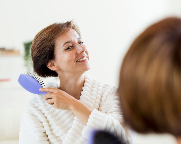 Mulher de roupão escovando o cabelo no espelho