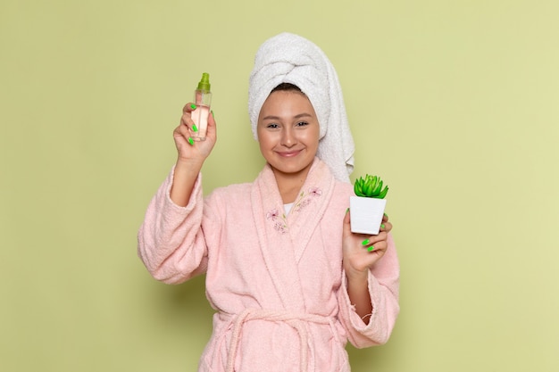 Mulher de roupão rosa segurando um spray e uma planta