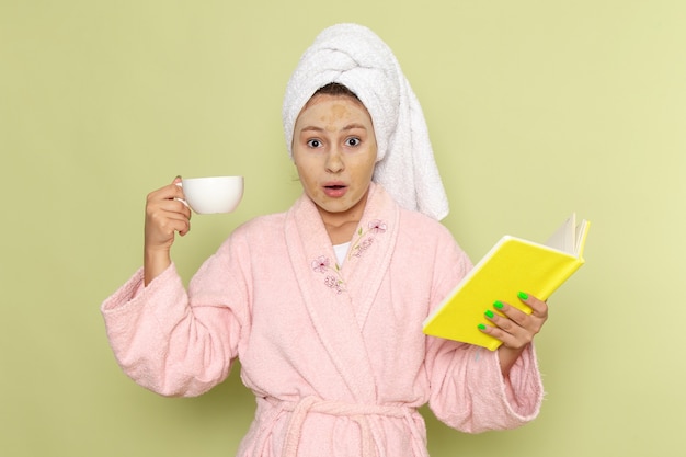 Mulher de roupão rosa tomando café e lendo livro