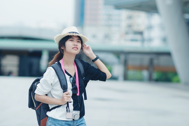 Mulher de sorriso que anda fora, jovem senhora que admira a vista da cidade com passagem e construções no fundo.