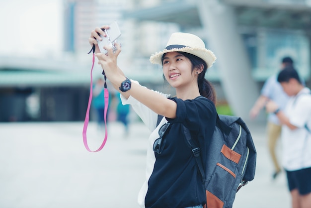 Mulher de sorriso que anda fora, jovem senhora que admira a vista da cidade com passagem e construções no fundo.