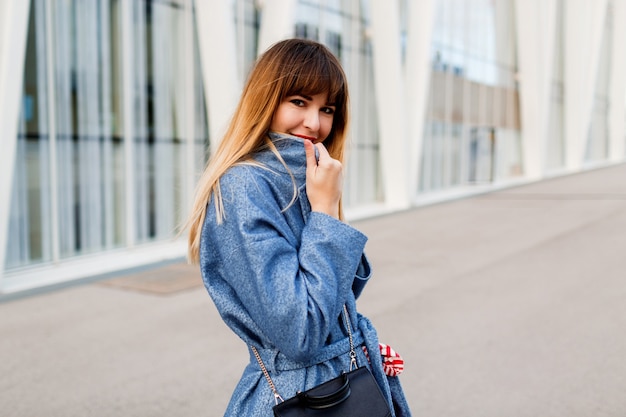 Mulher de sucesso posando perto do moderno centro de negócios com casaco azul de lã.