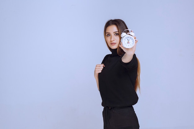 Mulher de suéter preto segurando o despertador e promovendo-o.