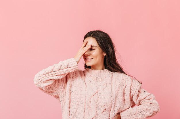 Mulher de suéter rosa posando em fundo isolado. Garota engraçada com sorriso faz facepalm.