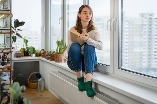 Mulher de tiro completo lendo em casa perto do aquecedor