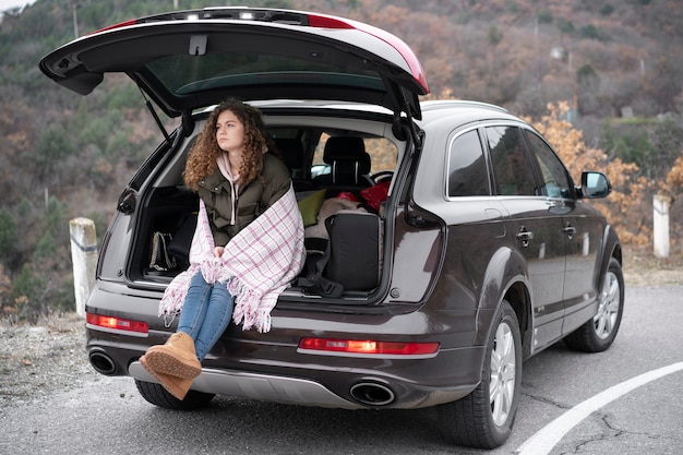 Mulher de tiro completo sentada no porta-malas do carro