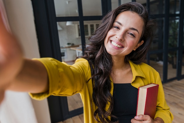 Mulher de tiro médio com livro tomando uma selfie