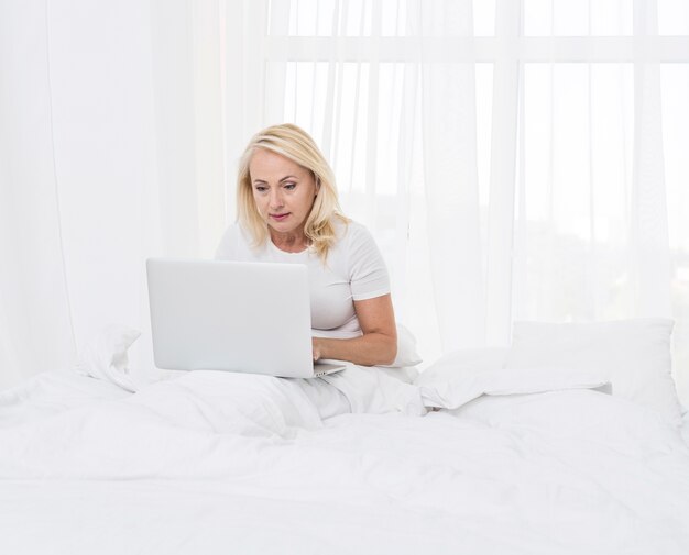 Mulher de tiro médio com o laptop na cama