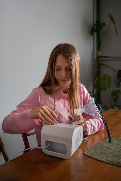 Mulher de tiro médio usando nebulizador em casa