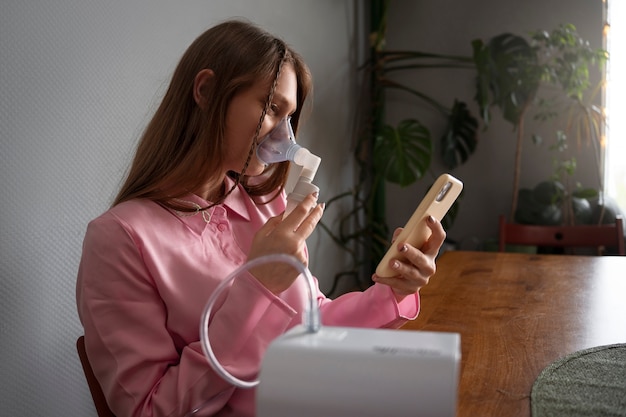 Mulher de tiro médio usando nebulizador em casa