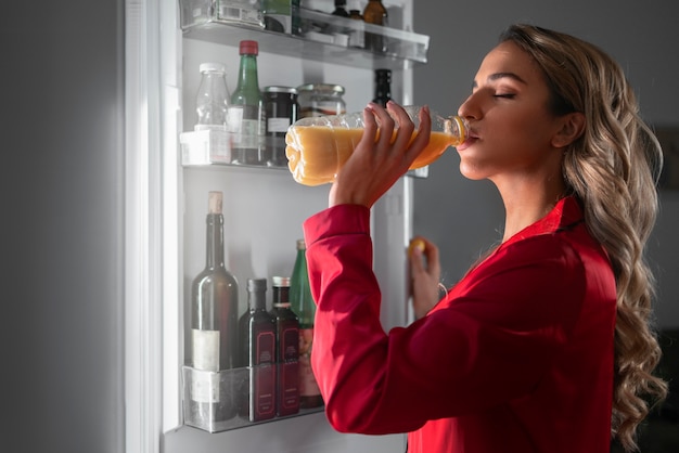 Mulher de tiro médio verificando a geladeira à noite