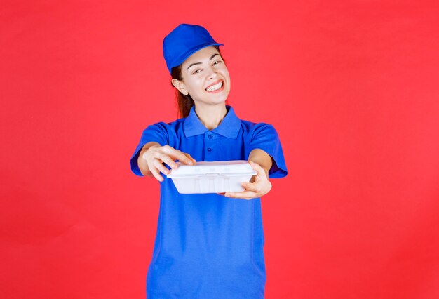 Mulher de uniforme azul segurando uma caixa de plástico branca para levar para entrega.