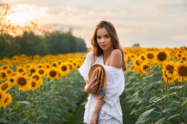 Mulher de vestido branco de verão posando no campo de girassol