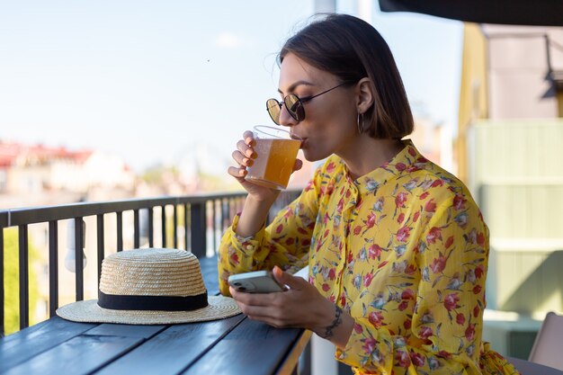 Mulher de vestido em um café de verão tomando um copo de cerveja legal de kombuchá