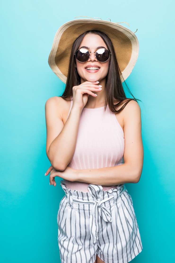 Foto grátis mulher de viagens de verão com chapéu e óculos de sol, pronto para a viagem de festa e festa isolada na parede azul. garota sorridente atraente pensando em férias. clima de verão.