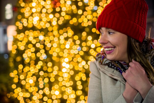 Mulher de vista lateral no mercado festivo de Natal à noite Mulher feliz olhando para cima com luz de Natal à noite