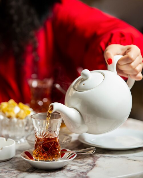 Mulher derramando chá preto do bule de chá em vidro armudu