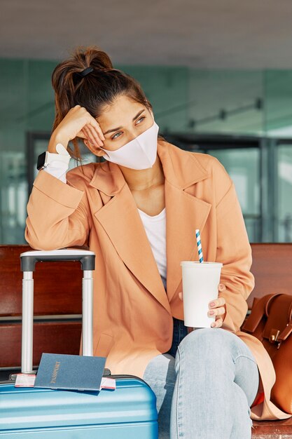 Foto grátis mulher descansando sobre a bagagem enquanto usava máscara médica no aeroporto durante a pandemia