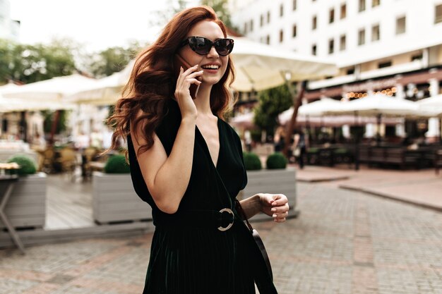 Mulher descolada de vestido escuro falando ao telefone