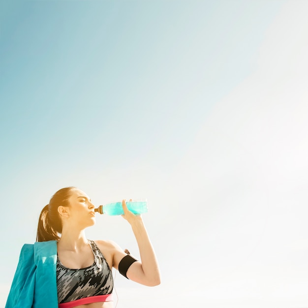 Mulher desportiva beber da garrafa no fundo do céu