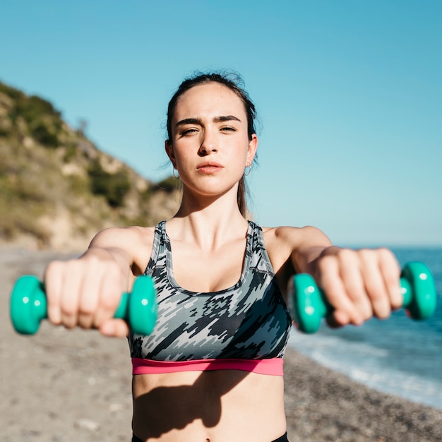 Mulher desportiva de treinamento com halteres na praia