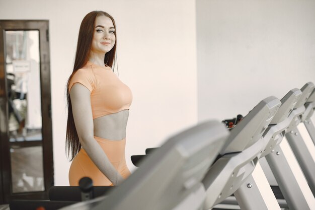 Mulher desportiva, exercitando-se em uma academia. Ela está em uma esteira. Desgaste ativo laranja.