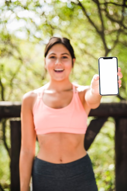 Mulher desportiva mostrando modelo de smartphone ao ar livre