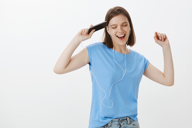 Foto grátis mulher despreocupada dançando e cantando, ouvindo música com fones de ouvido no celular