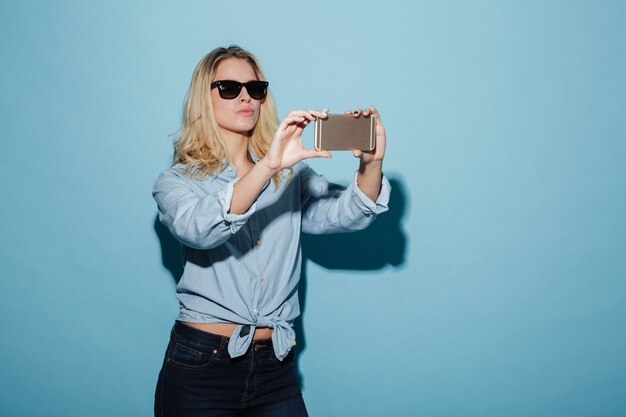 Mulher despreocupada de camisa e óculos de sol fazendo selfie em smartphone