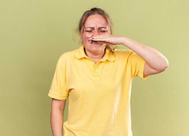 Mulher doente com camisa amarela se sentindo muito mal, gripe e frio, enxugando o nariz escorrendo