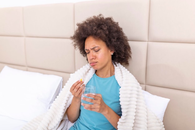 Mulher doente do milênio tomando remédio analgésico para aliviar a dor de estômago sente-se na cama de manhã Mulher doente deitada na cama com febre alta Gripe fria e enxaqueca