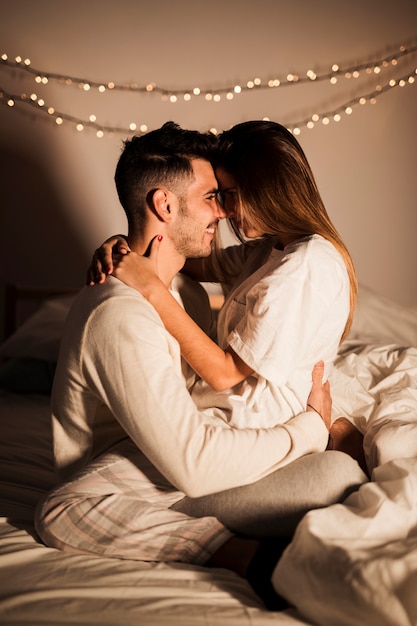 Mulher e homem sorridente, abraçando na cama no quarto escuro