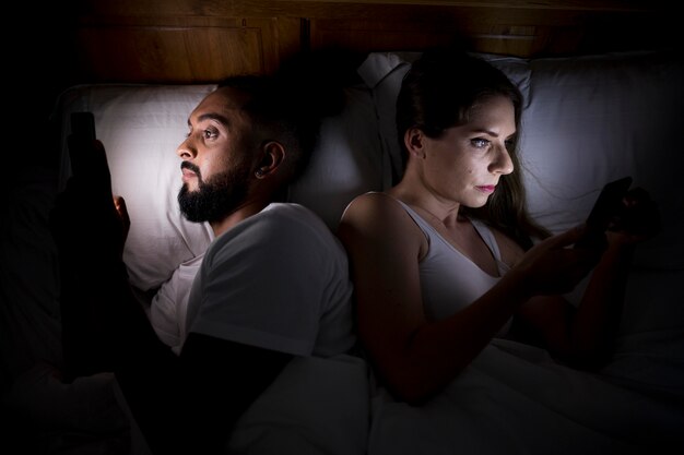 Mulher e homem verificando seus telefones antes de dormir