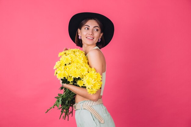 Mulher elegante com chapéu, abraçando um grande buquê de ásteres amarelos, clima de primavera, espaço isolado e calmo e sorridente