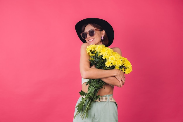 Foto grátis mulher elegante com chapéu e óculos escuros, abraçando um grande buquê de ásteres amarelos, clima de primavera, calmo e sorridente espaço isolado