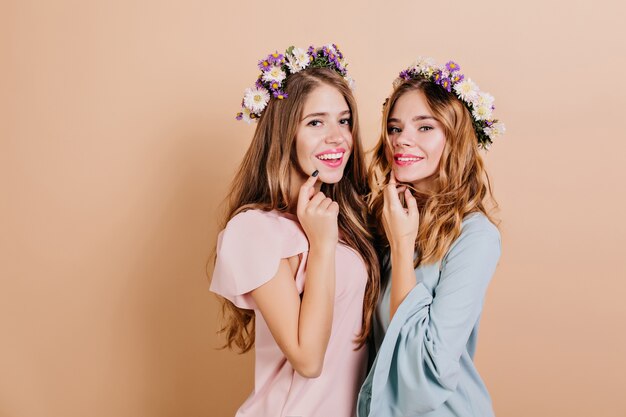Mulher elegante com grinalda de flores expressando felicidade durante a sessão de fotos com a irmã
