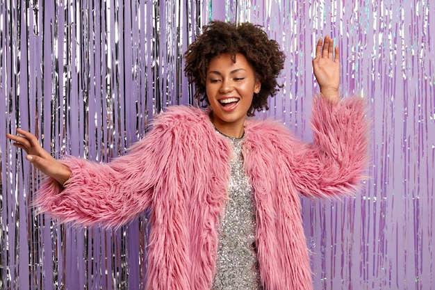 Mulher elegante com penteado afro dançando na boate, se divertindo na discoteca, vestida com roupas elegantes