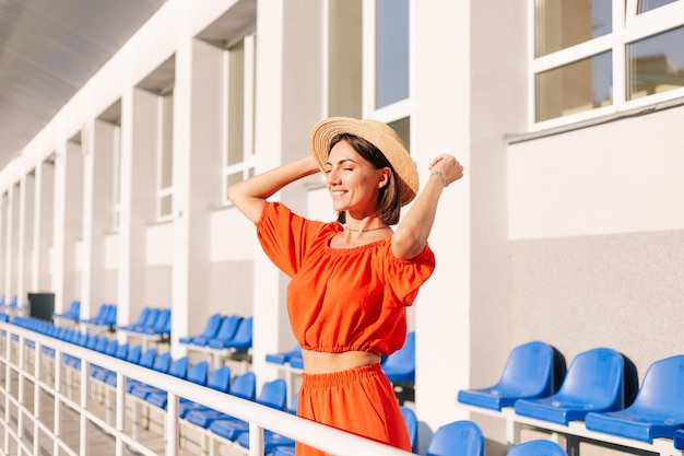 Foto grátis mulher elegante com roupas laranja ao pôr do sol no estádio da ciclovia posando